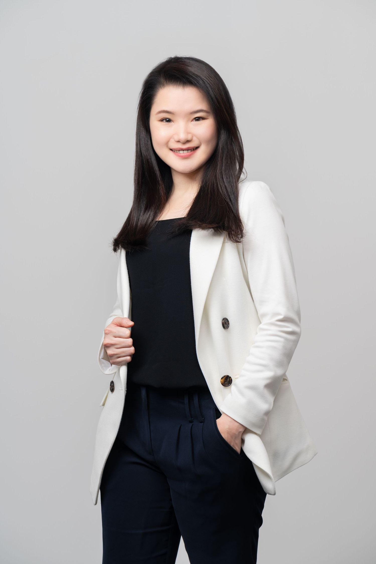 Professional studio portrait showing someone in a crisp white blazer and black outfit against a gray background.