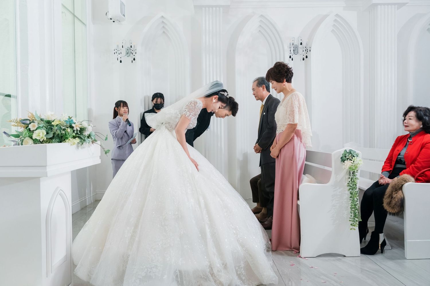 Wedding celebration in a white chapel-style venue with guests and decorative floral arrangements.