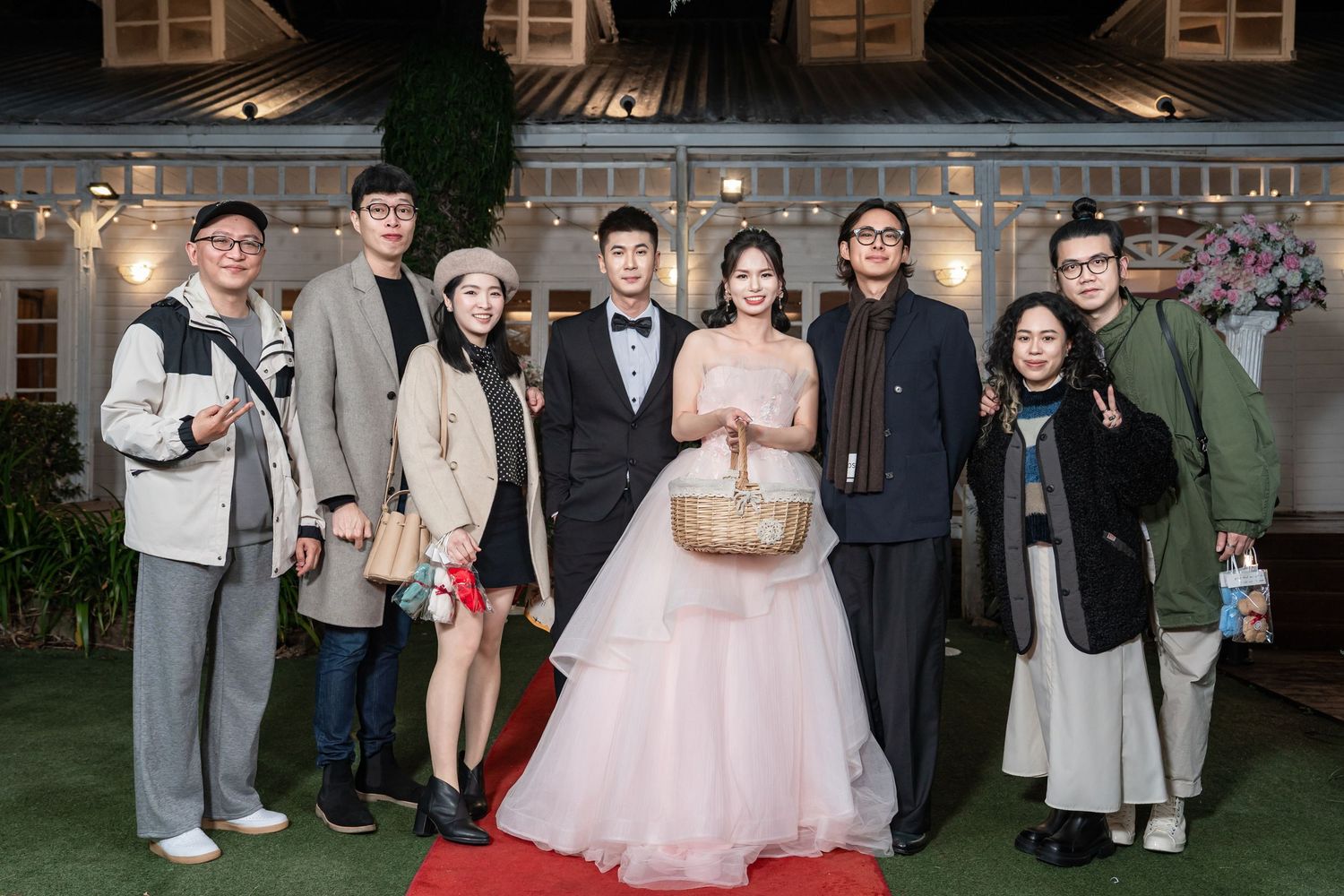 Wedding celebration scene with guests posing together at outdoor venue with architectural backdrop.