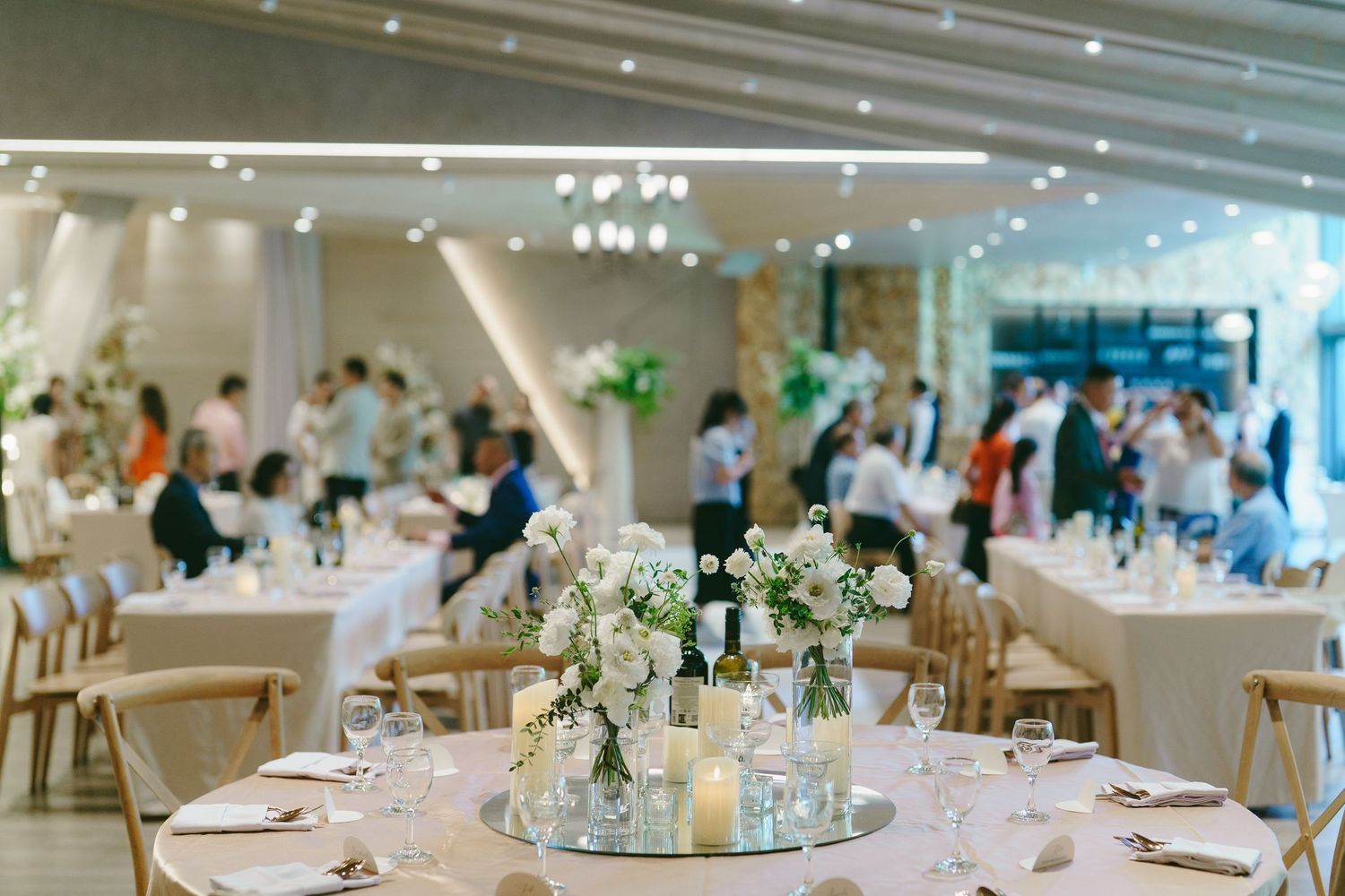An elegant wedding reception ballroom decorated with white linens, floral centerpieces and round dining tables.