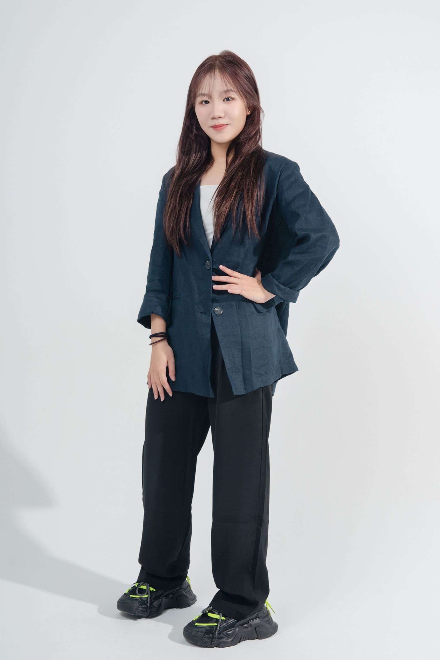 A person poses in an oversized black business suit and chunky sneakers against a white studio background.