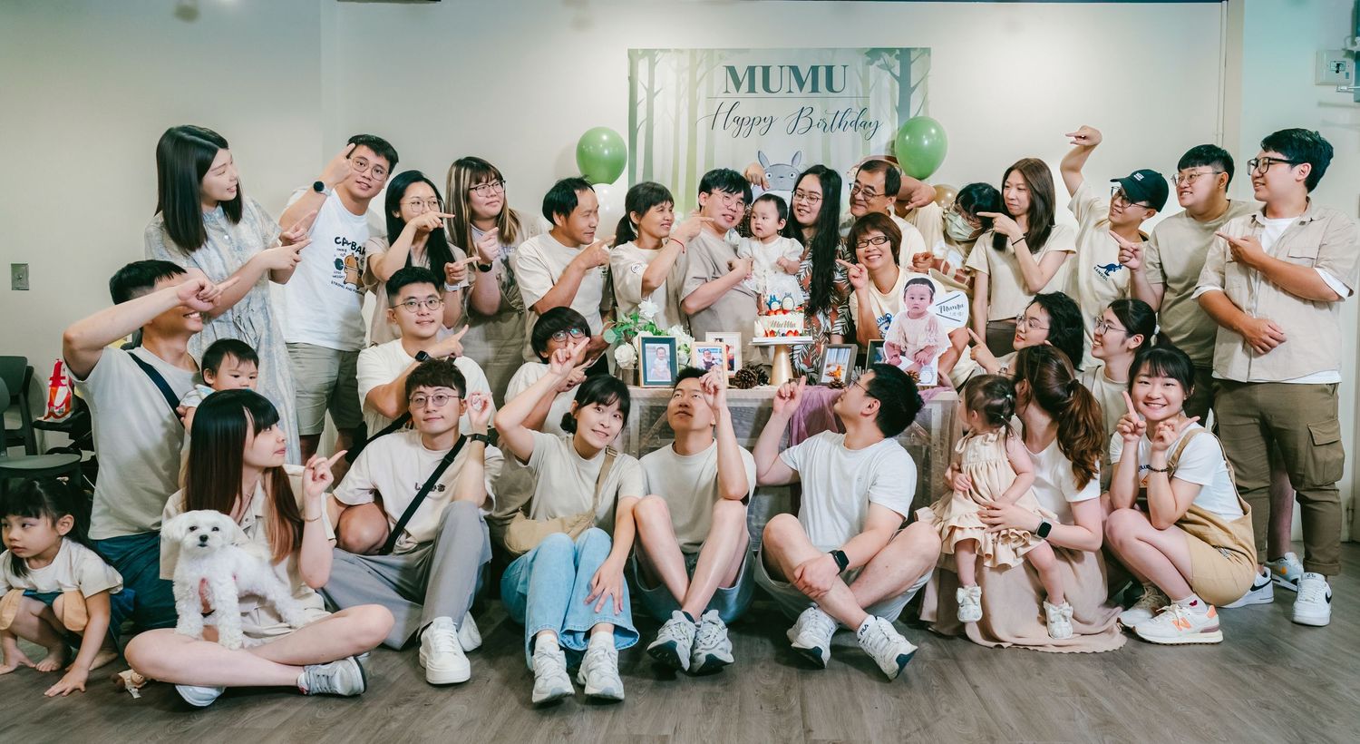 A large group poses together in casual summer outfits against a white wall with a Mumu sign above them.