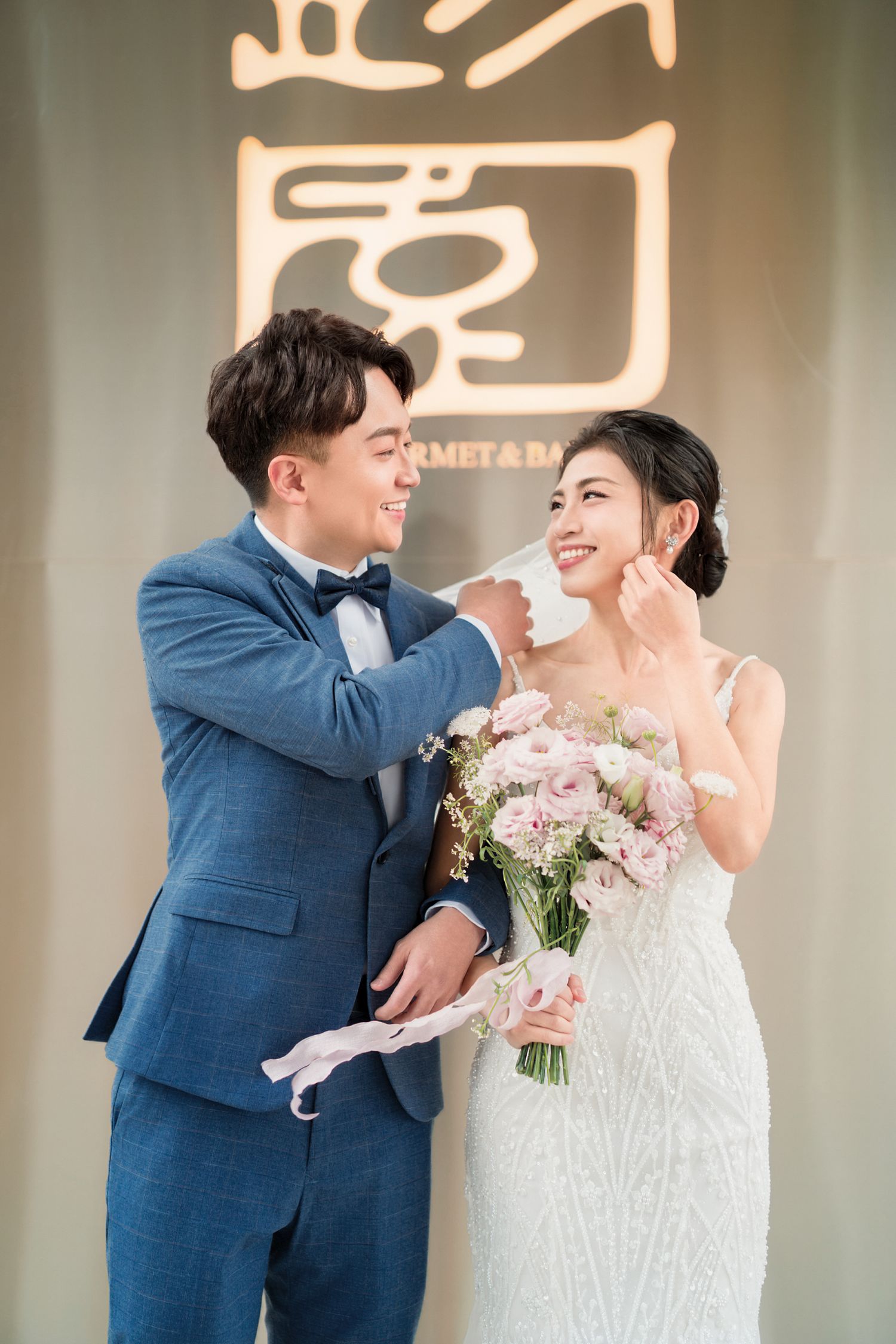 A newlywed couple in formal wedding attire share an intimate moment while holding a bouquet of pink and white flowers.