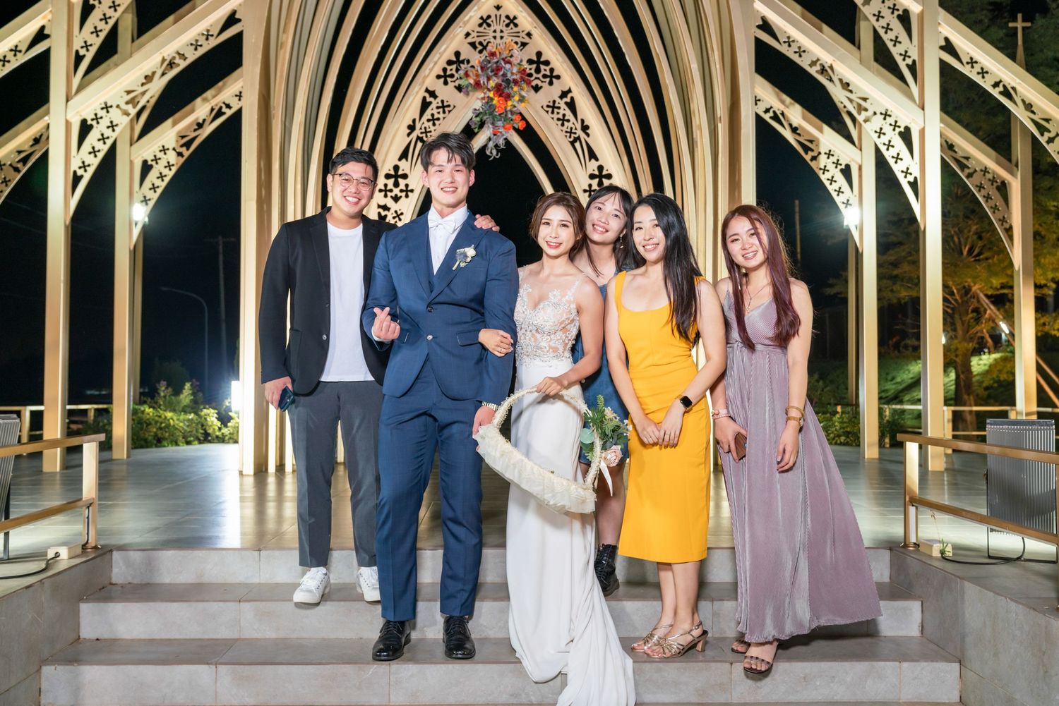 Group photo of wedding guests standing together under an ornate gothic archway at night.