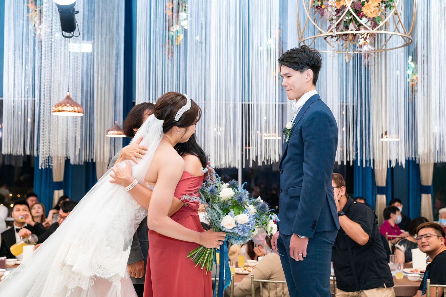 A wedding reception moment at an elegant venue with silver metallic streamers and chandelier decorations.