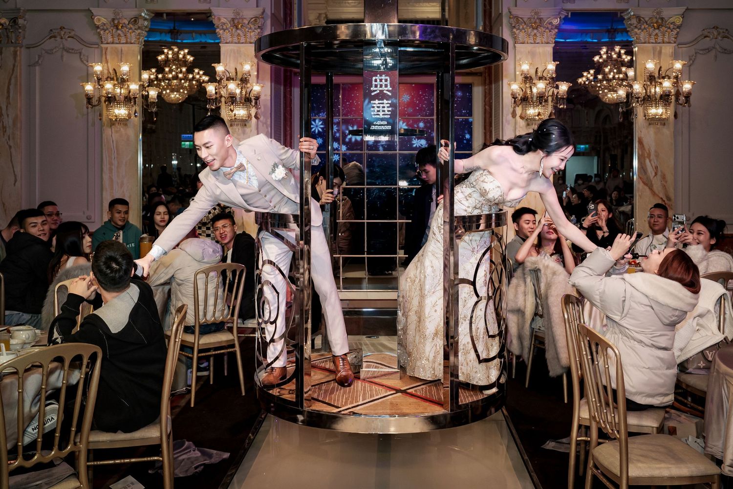 Wedding guests dance and celebrate during an evening reception in an elegant ballroom with chandeliers.