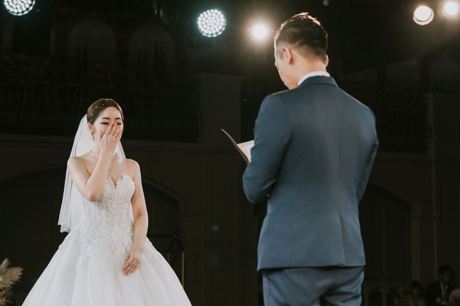 A couple exchanging vows during a wedding ceremony under stage lighting.