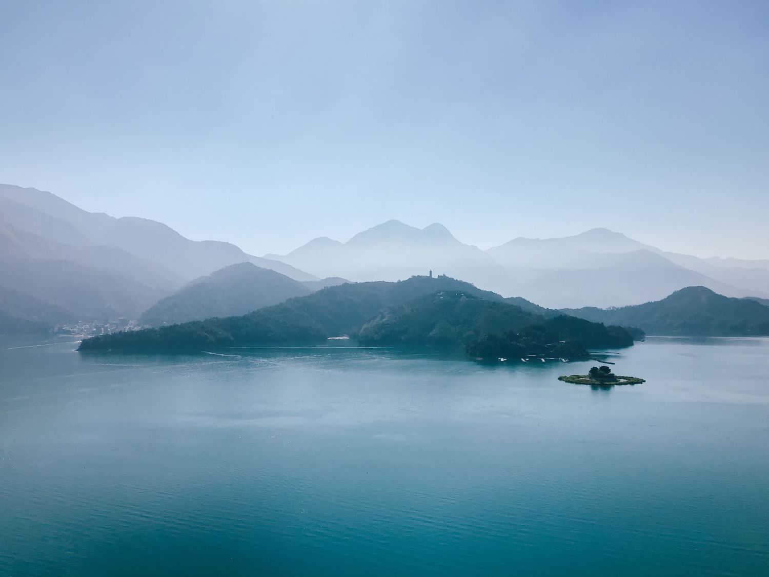 A misty morning view of Sun Moon Lake in Taiwan shows mountains and islands emerging from tranquil turquoise waters.