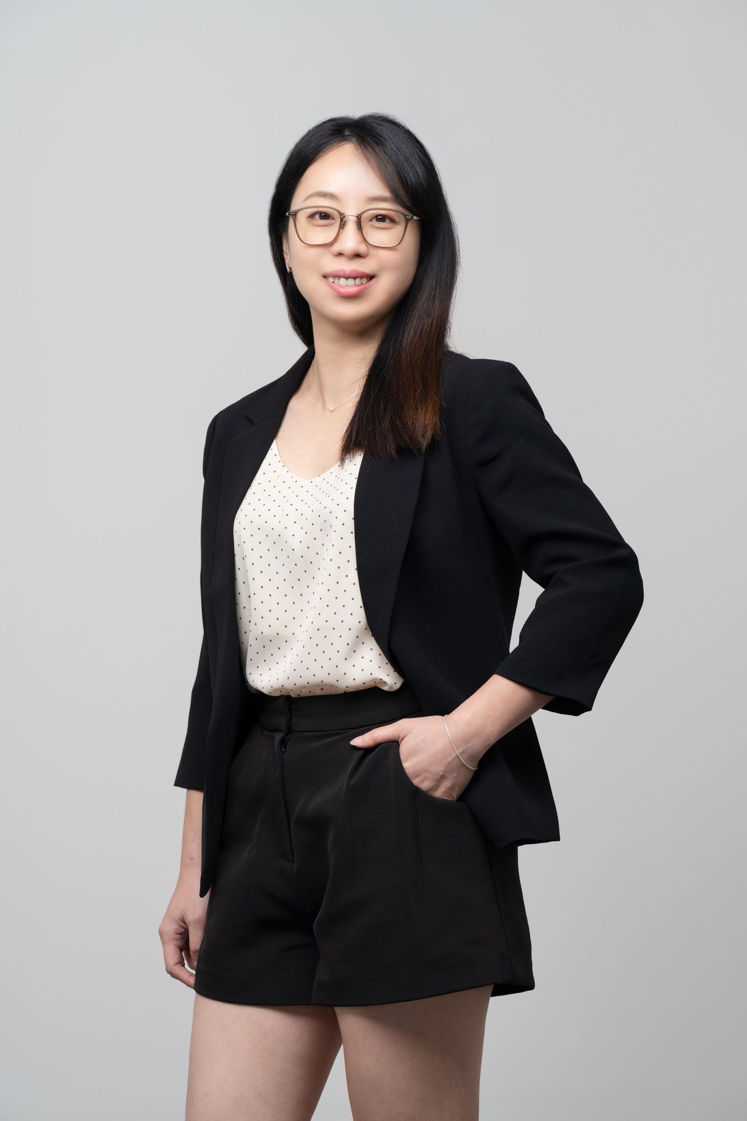 Professional fashion portrait showing a polished business casual outfit with black blazer and shorts over white polka dot top.