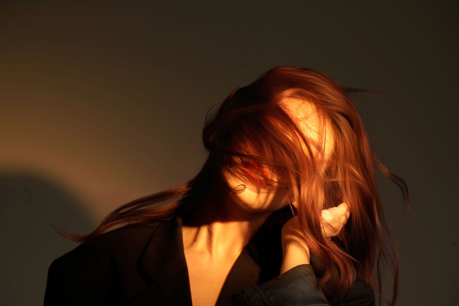 Dramatic side profile silhouette of someone with flowing red hair against dark background illuminated by warm light.