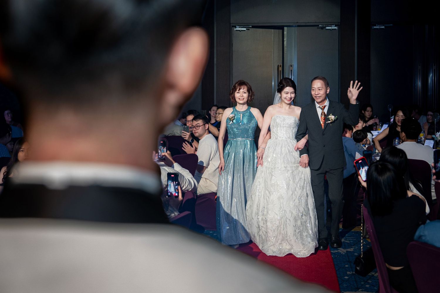 Wedding party poses together at an elegant celebration with guests in the background.