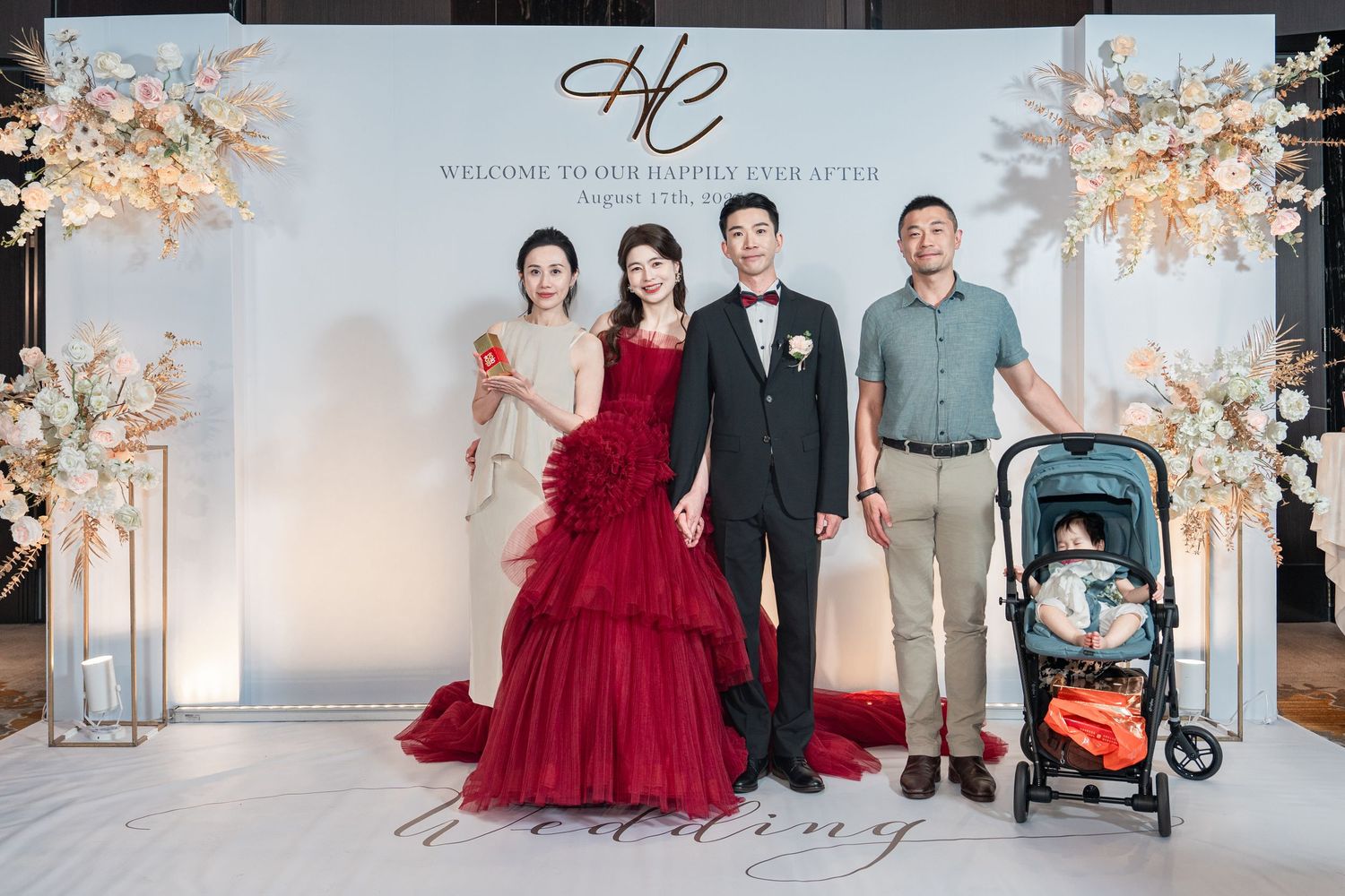 A formal event with wedding decor featuring cherry blossom trees and a group posing in front of a monogram backdrop.