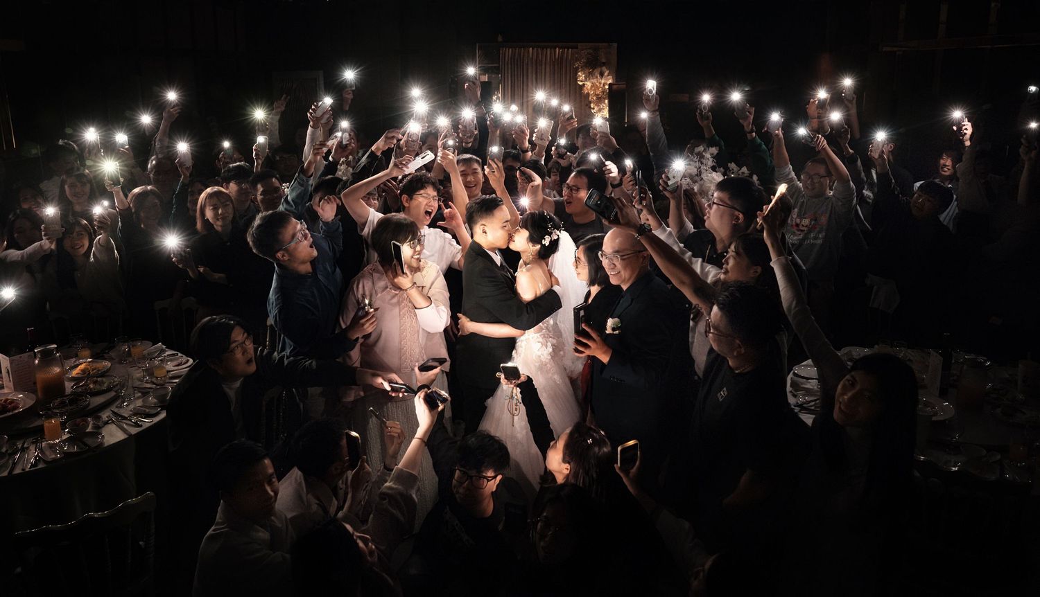 A crowd of concert-goers dances under string lights at a nighttime outdoor music event.