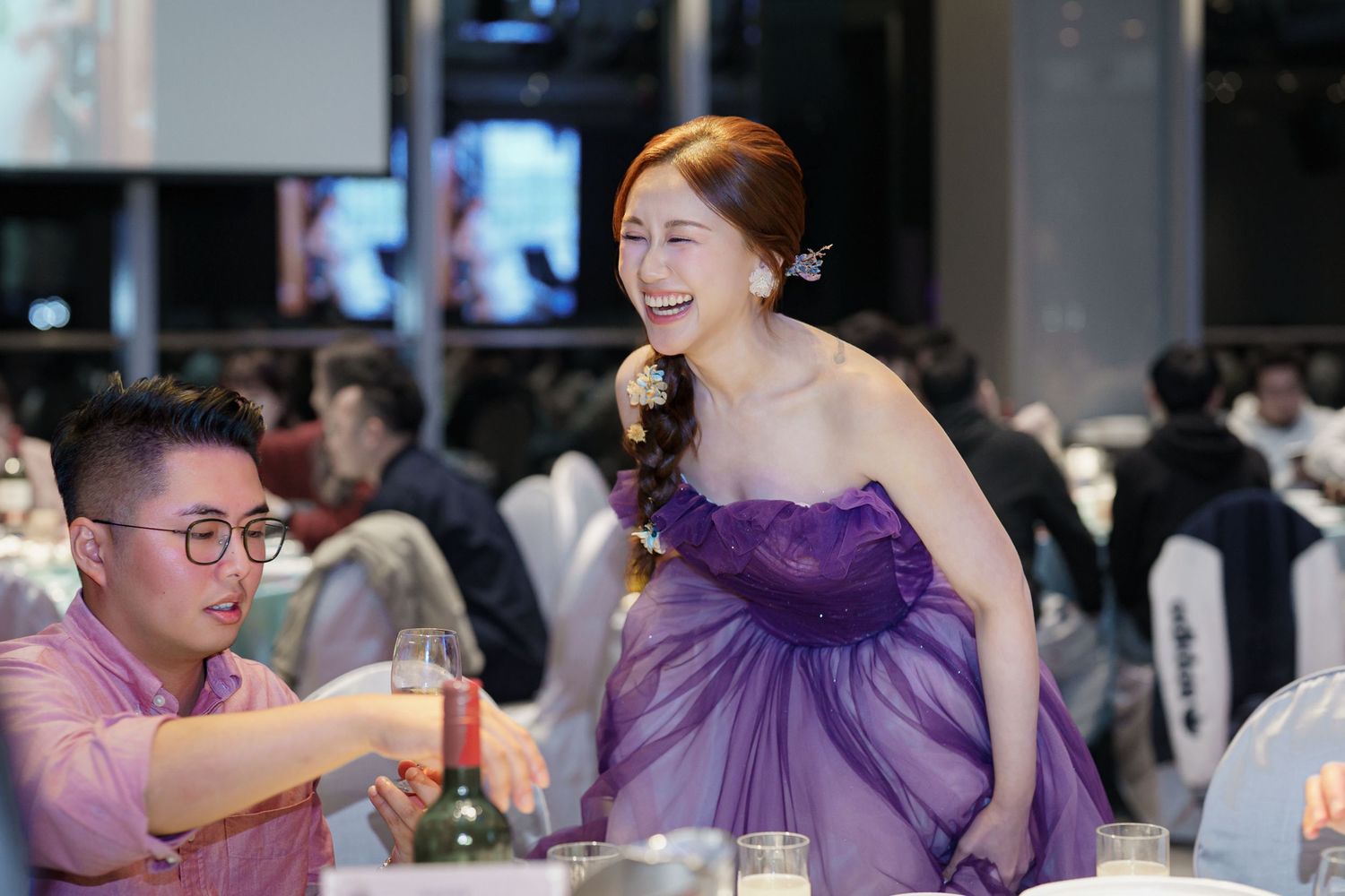 Wedding guests in purple attire celebrate joyfully during a reception at an indoor venue.