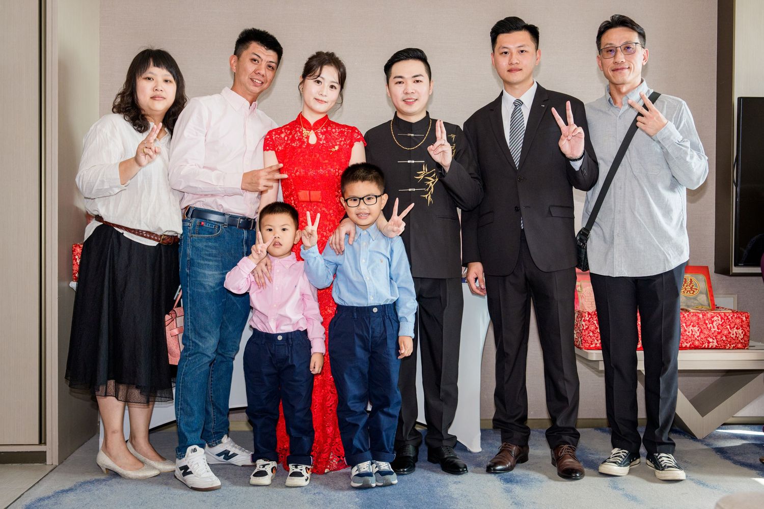 Family members in formal and casual attire pose together against a light colored wall for a group photo.