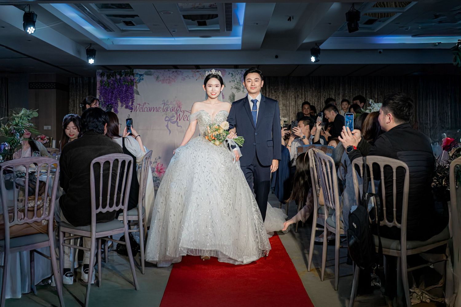 A wedding reception venue features elegant white chairs and decorative lighting for an indoor celebration.