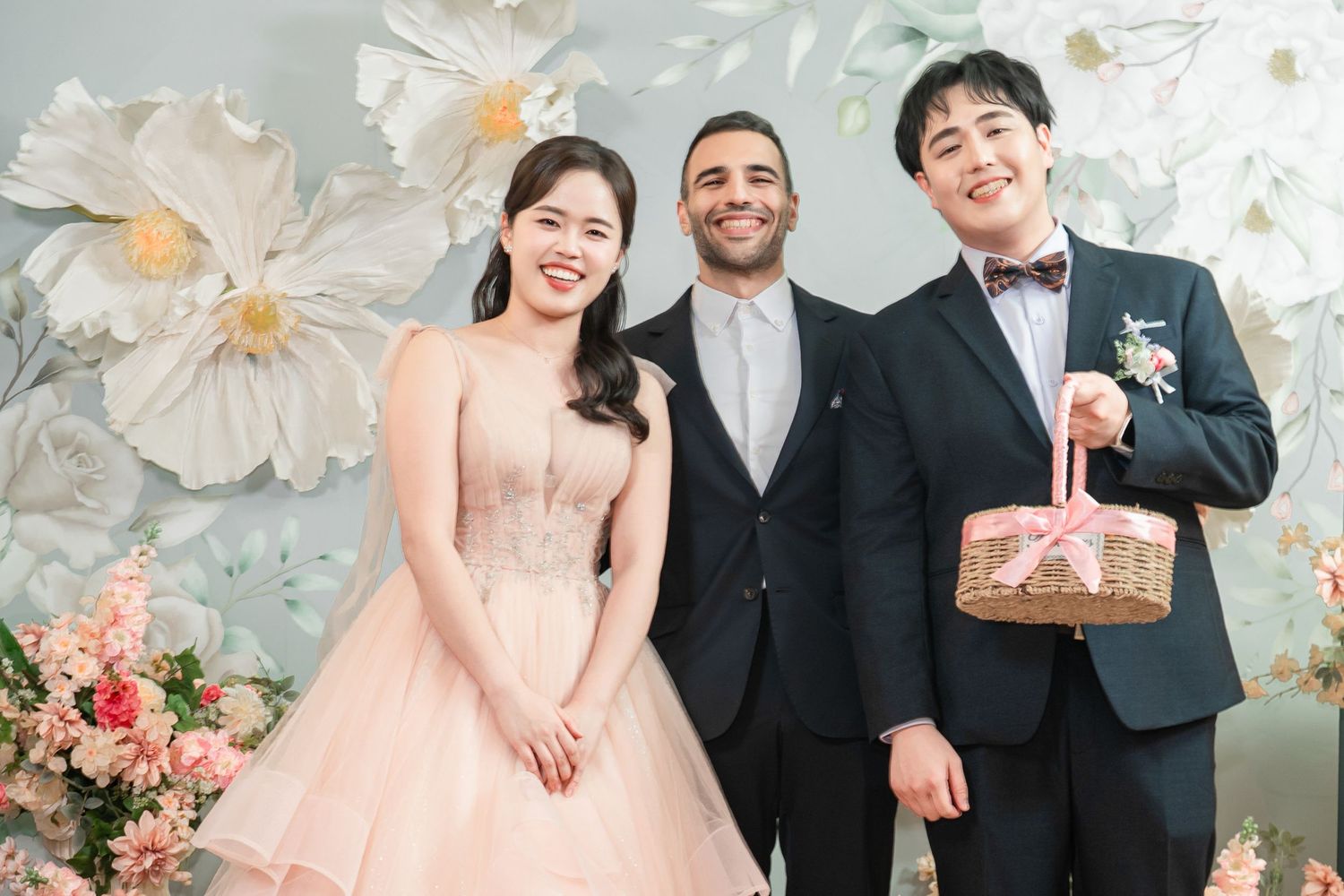 Wedding party in formal attire poses together against floral backdrop at elegant celebration.