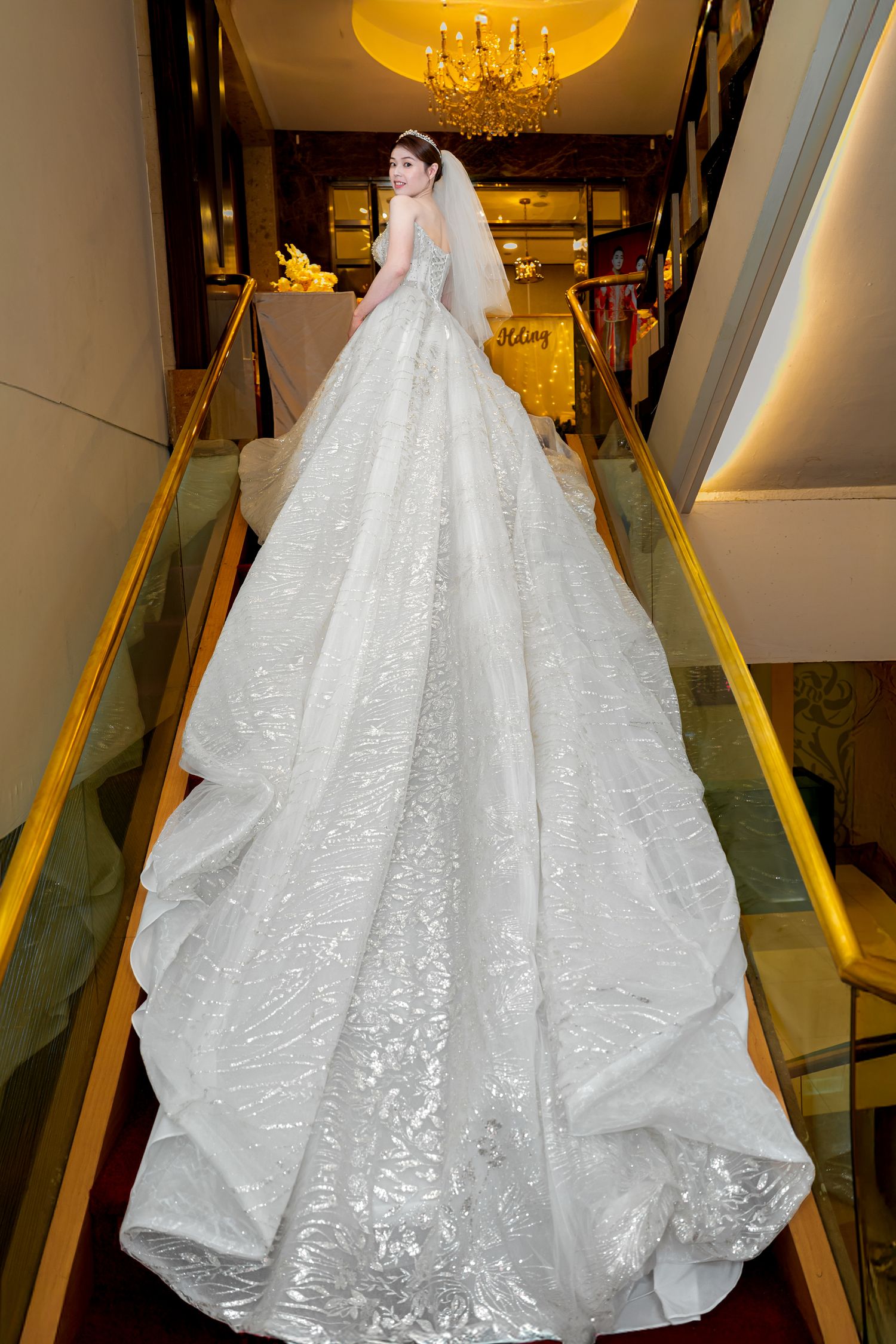 A stunning white wedding gown with intricate lace detailing and a dramatic cathedral train displayed in an elegant showroom.