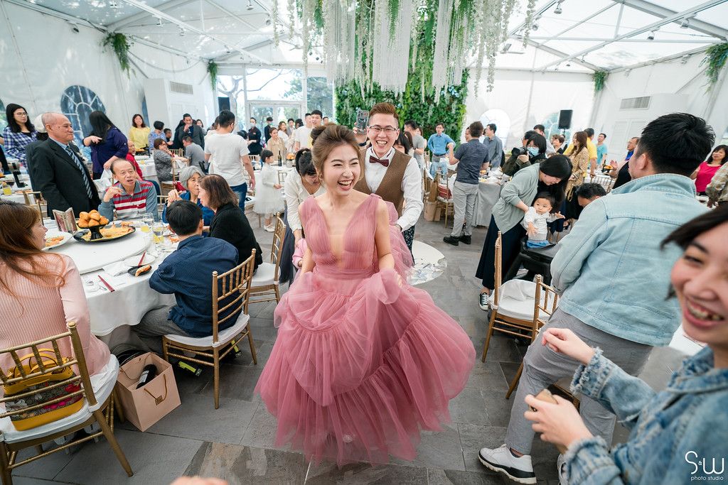 Guests enjoying a wedding reception in a modern greenhouse-style venue with trailing plants.