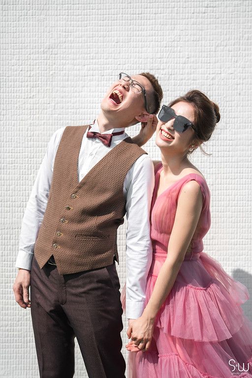 A fun portrait of a couple in formal wear making silly expressions against a white background.