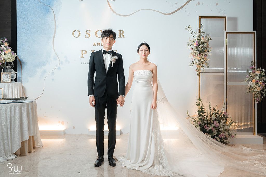Wedding couple posing against white backdrop with gold frames and floral decorations.