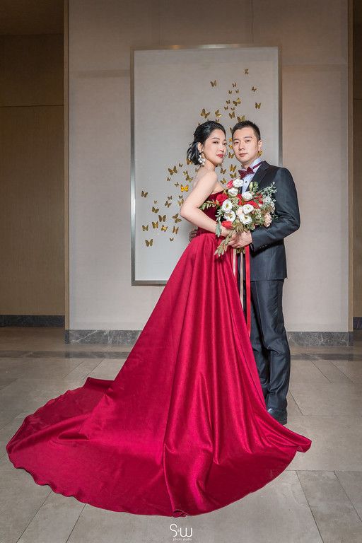 Romantic wedding portrait with couple in red gown and black tux against butterfly wall art.