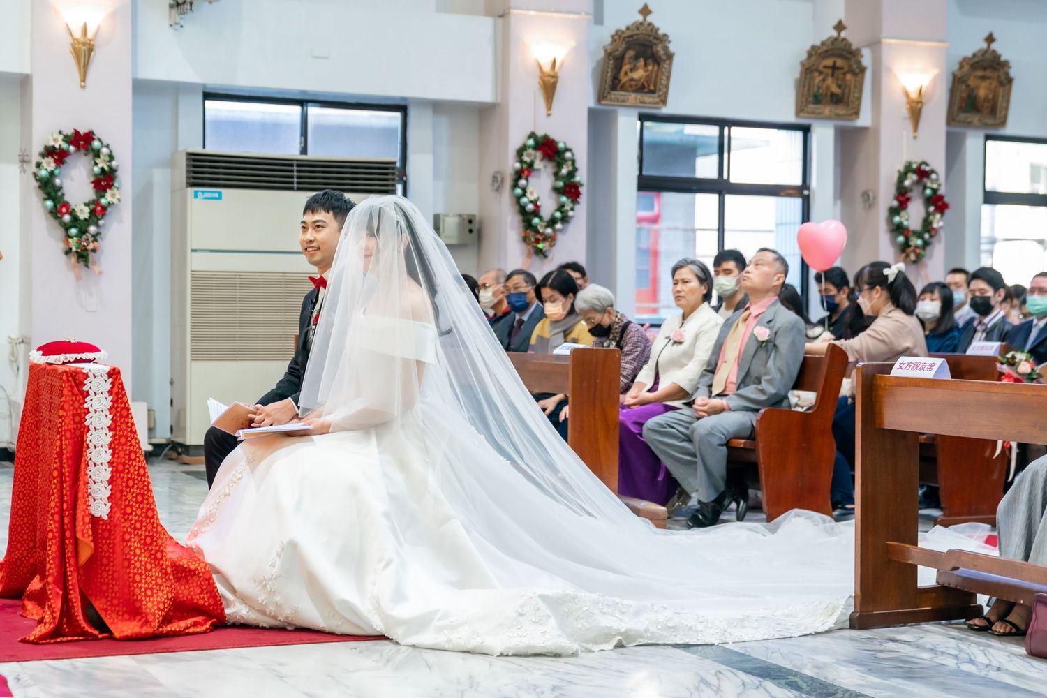 A wedding ceremony in progress with a long flowing white veil and red decorative elements.