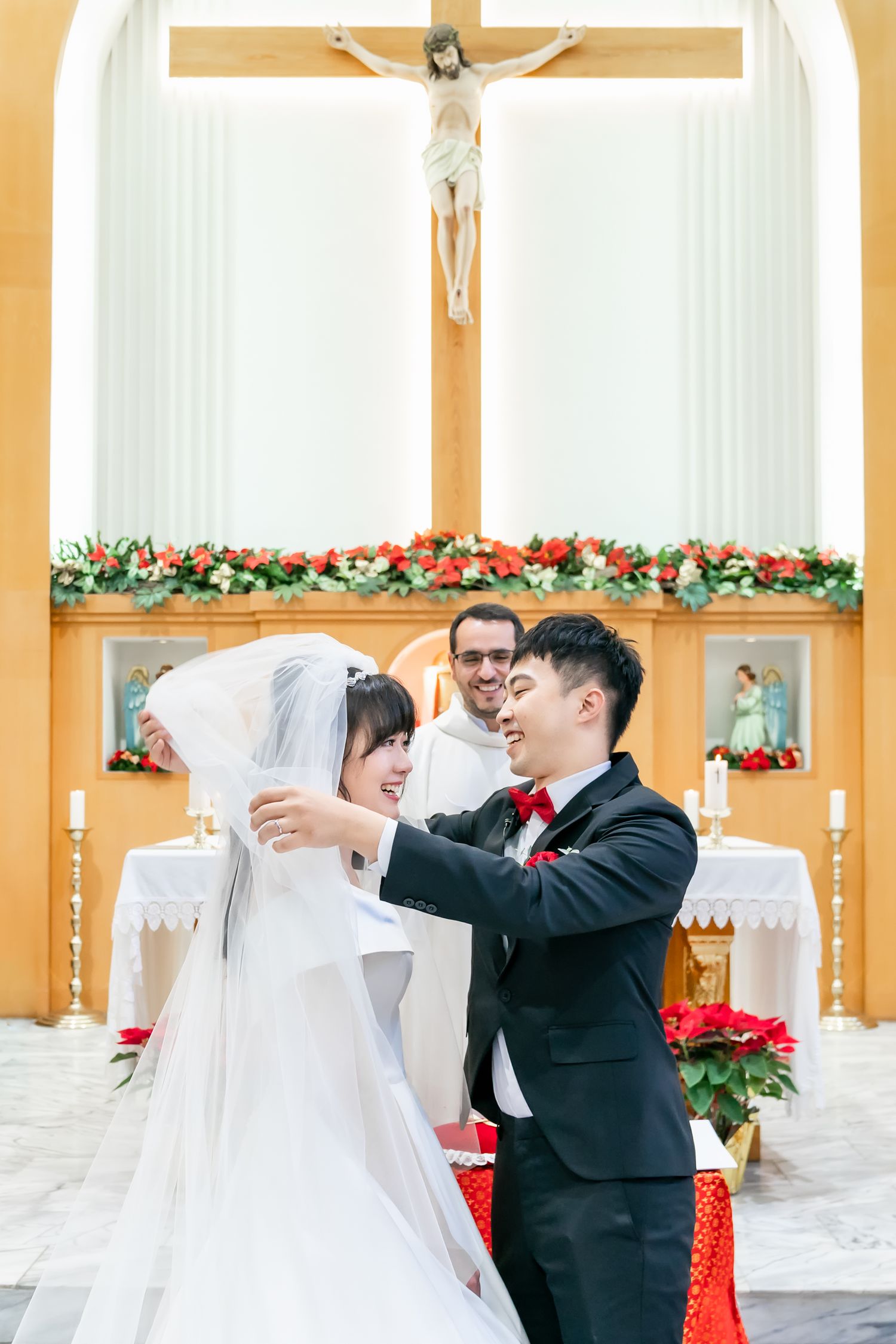 Joyful wedding moment captured in church with crucifix and floral decorations in background.