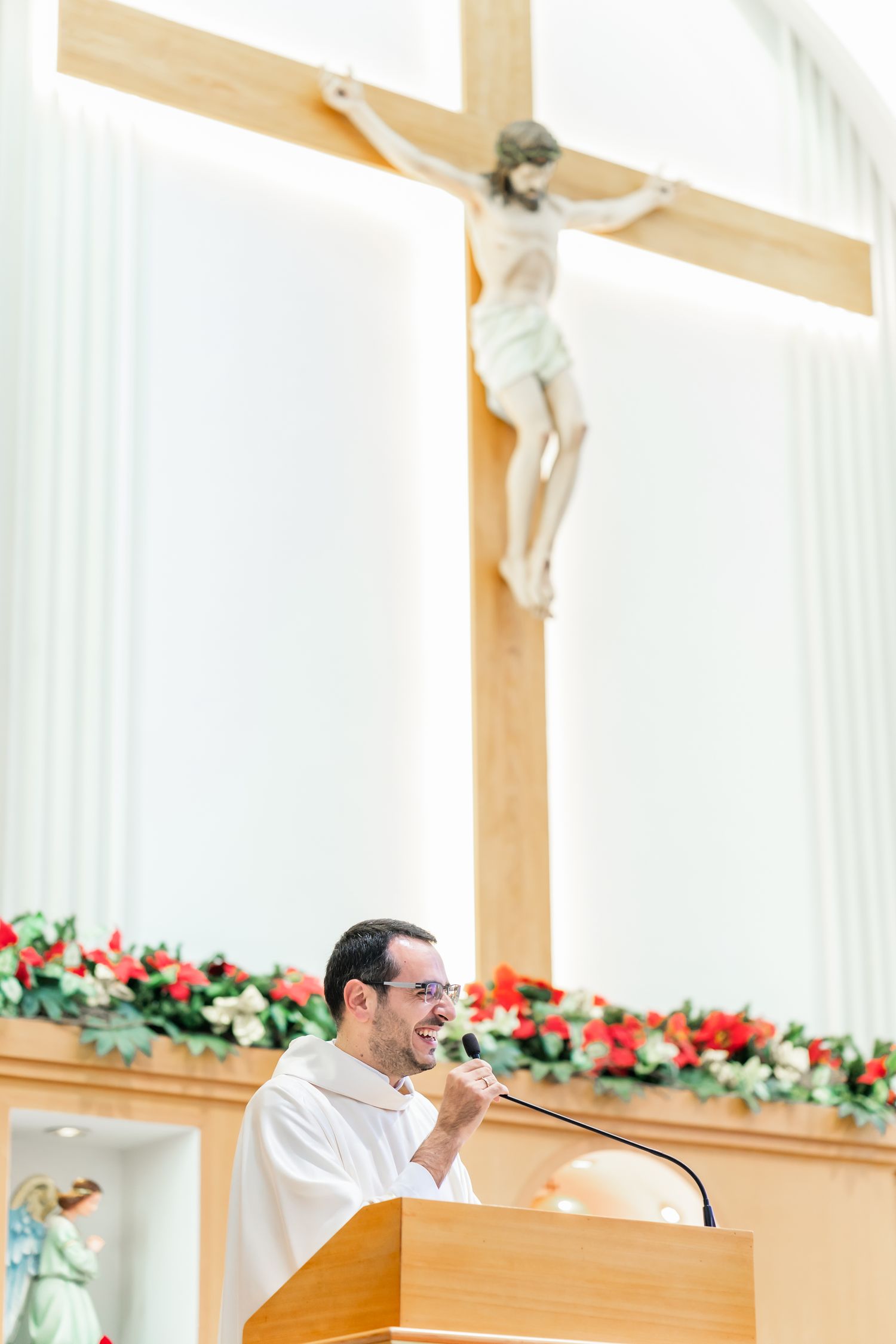 A wooden crucifix hangs above a podium decorated with red flowers in a church setting.