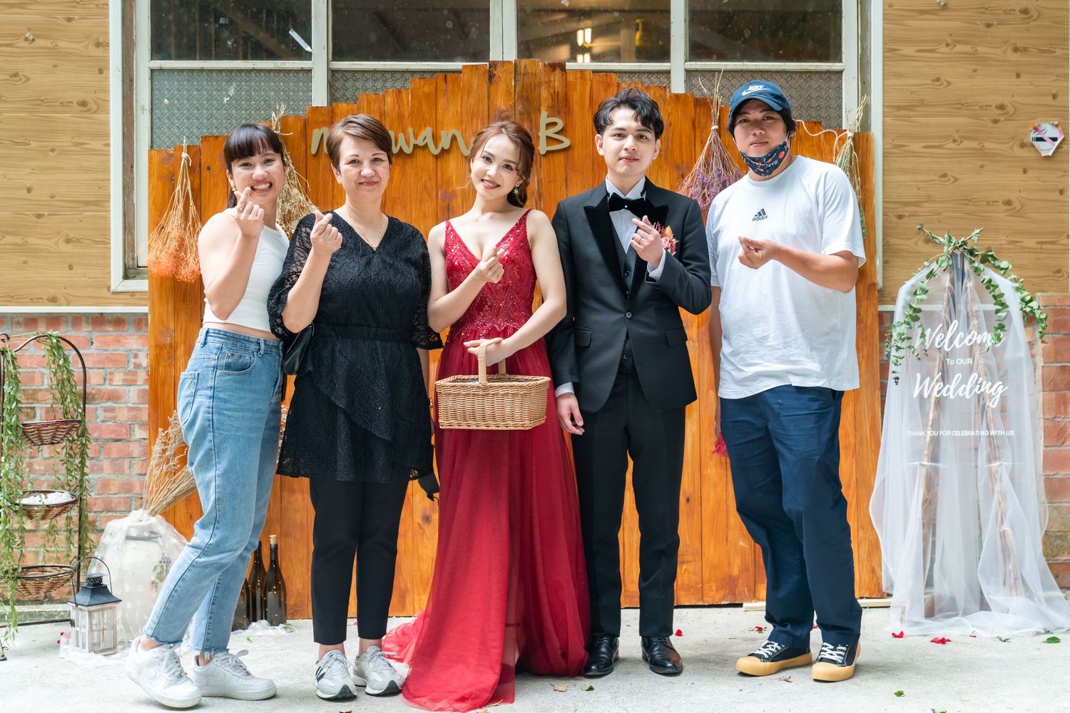 Group photo with casual and formal attire in front of orange backdrop with wedding decor.