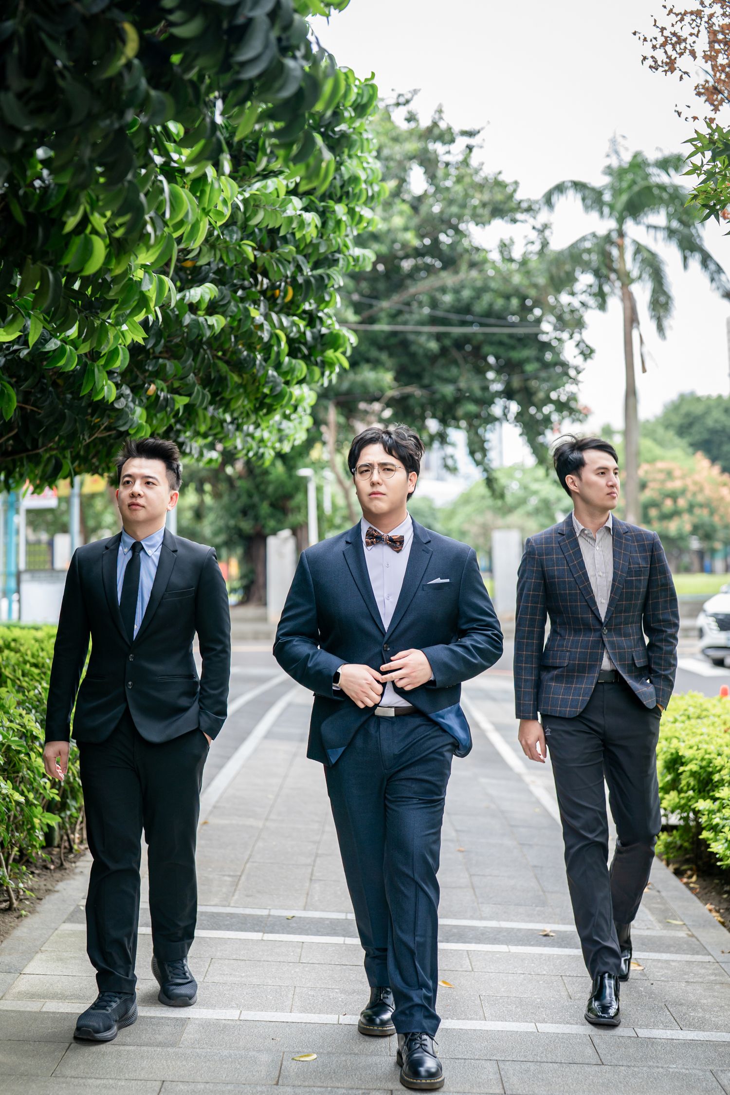 A group of groomsmen in dark suits walk together along a palm tree-lined pathway.