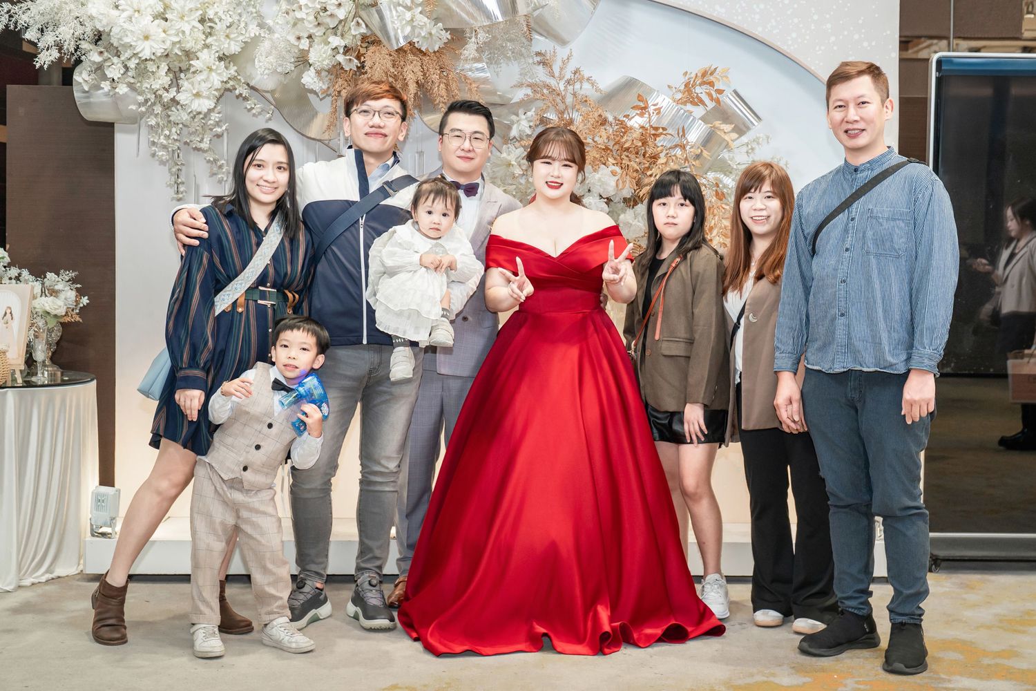 A group of people pose together at a formal event with a person wearing a stunning red ballgown as the centerpiece.