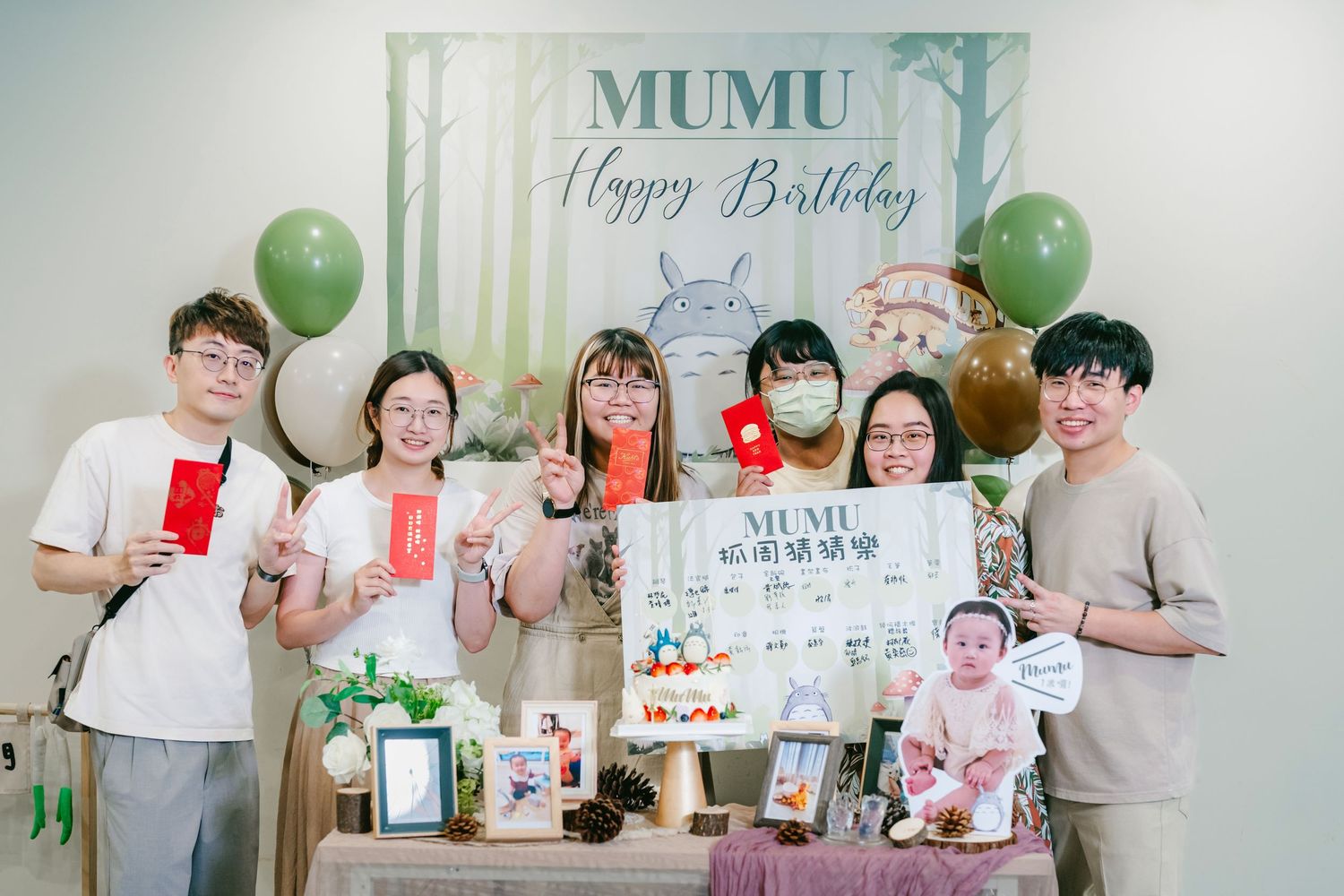 Birthday party decorations and guests gather around a dessert table with green balloons and a 'Happy Birthday' sign.