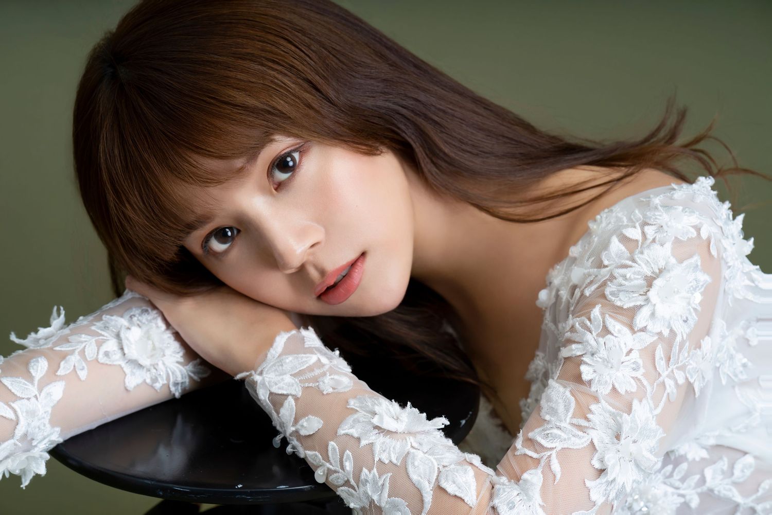 Portrait in elegant white lace sheer sleeve gown against green backdrop.
