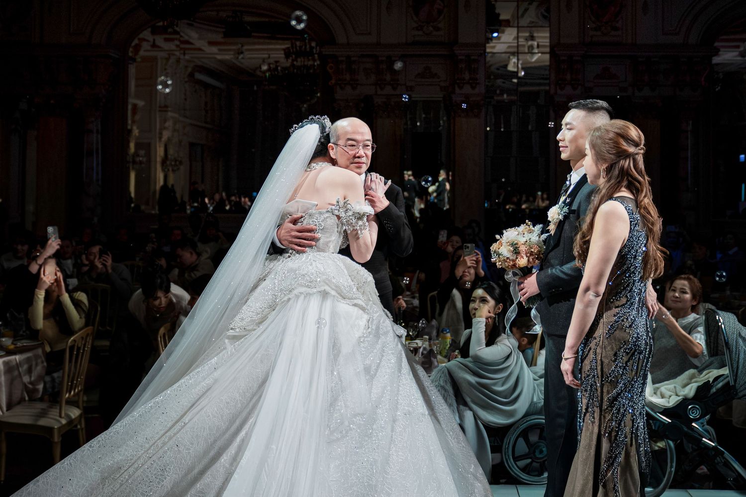 An emotional moment at a wedding ceremony with a bride in a voluminous white ball gown and veil embracing another person.