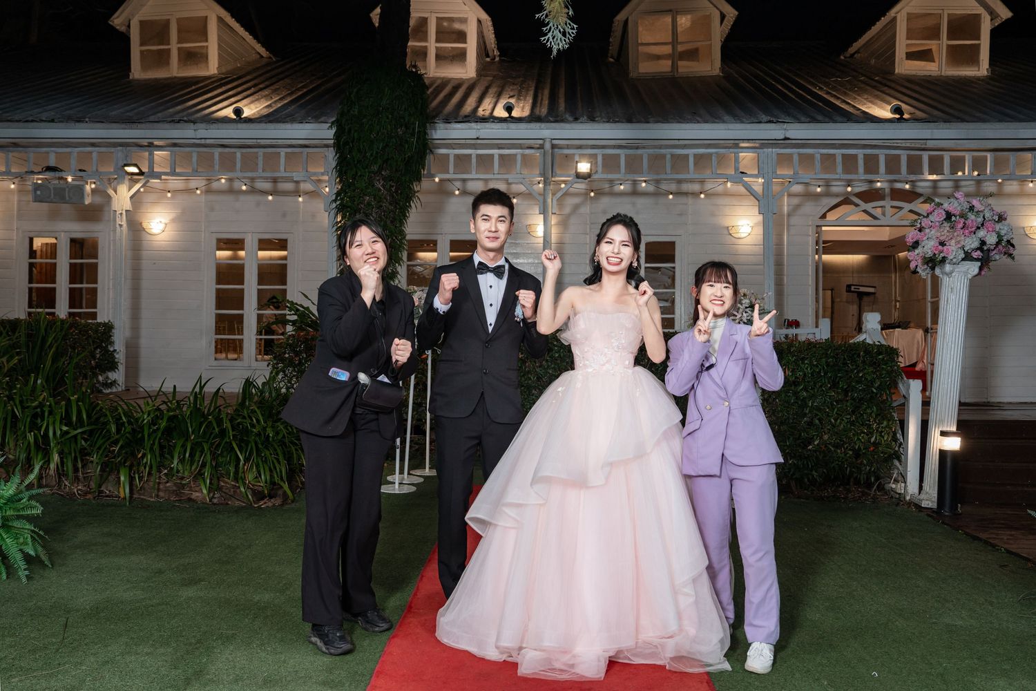 Wedding party members stand together outside an elegant venue during an evening celebration.