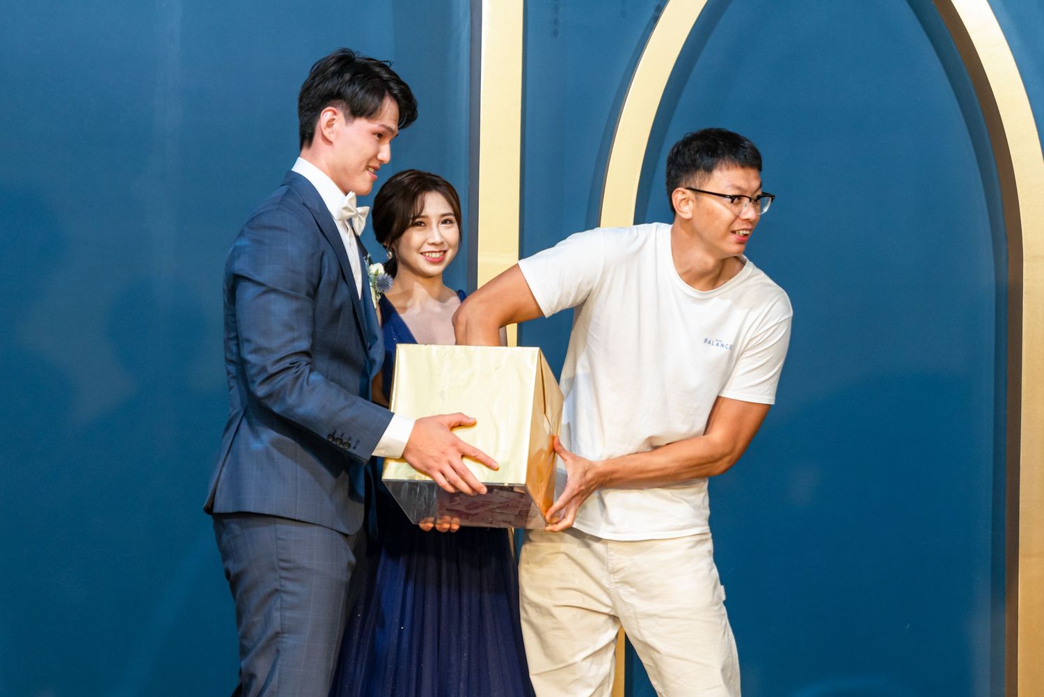 Three people stand in front of a blue wall with gold circular accents, holding a book or document together.