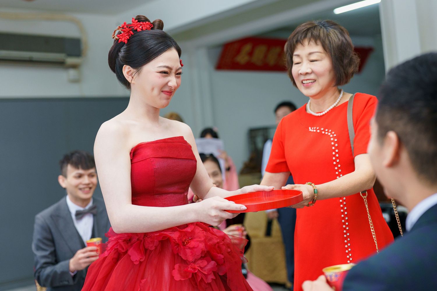 A bride in a red strapless gown receives a red envelope during a traditional Chinese wedding ceremony.