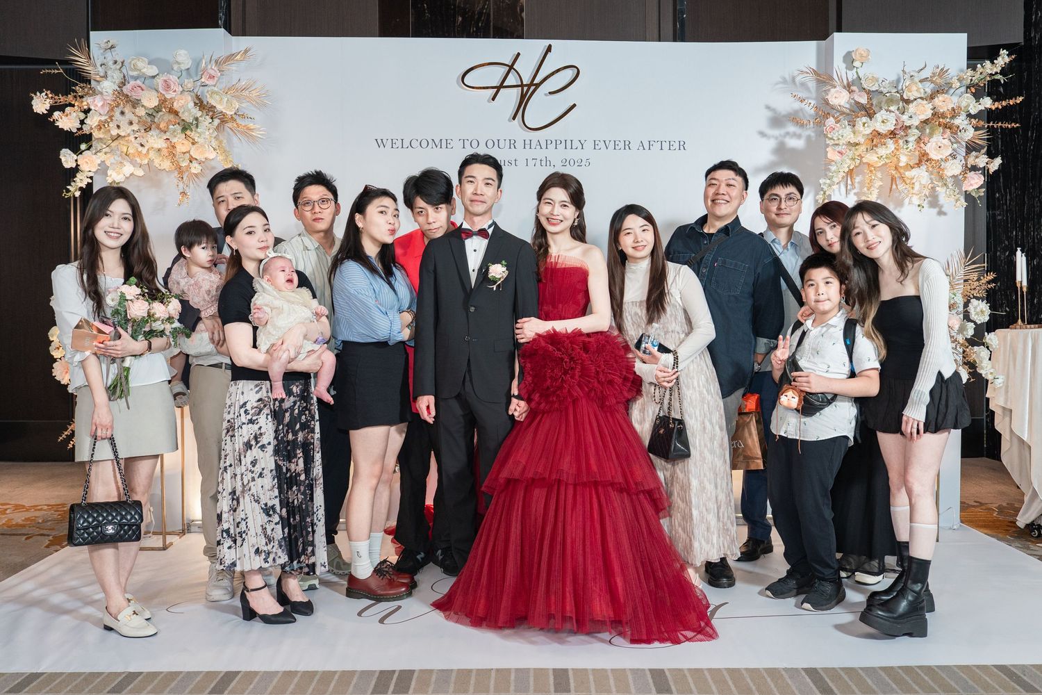 Family group poses at an elegant wedding reception with festive decorations and a stylish red gown as the centerpiece.