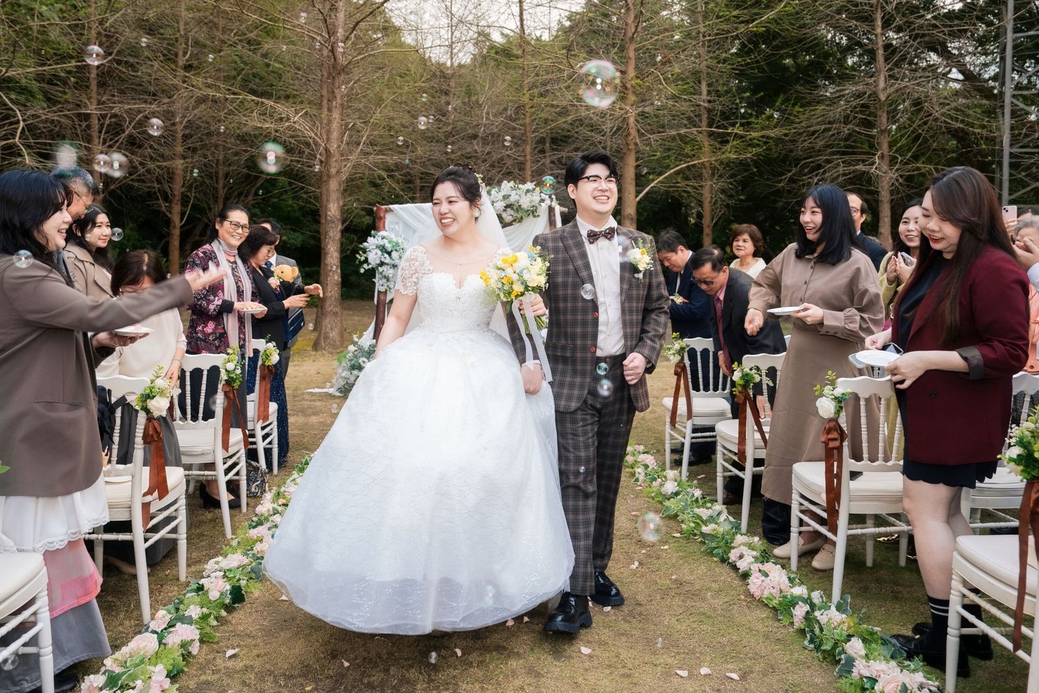 Outdoor wedding ceremony setup in a garden with white chairs and floral aisle decorations during a spring celebration.