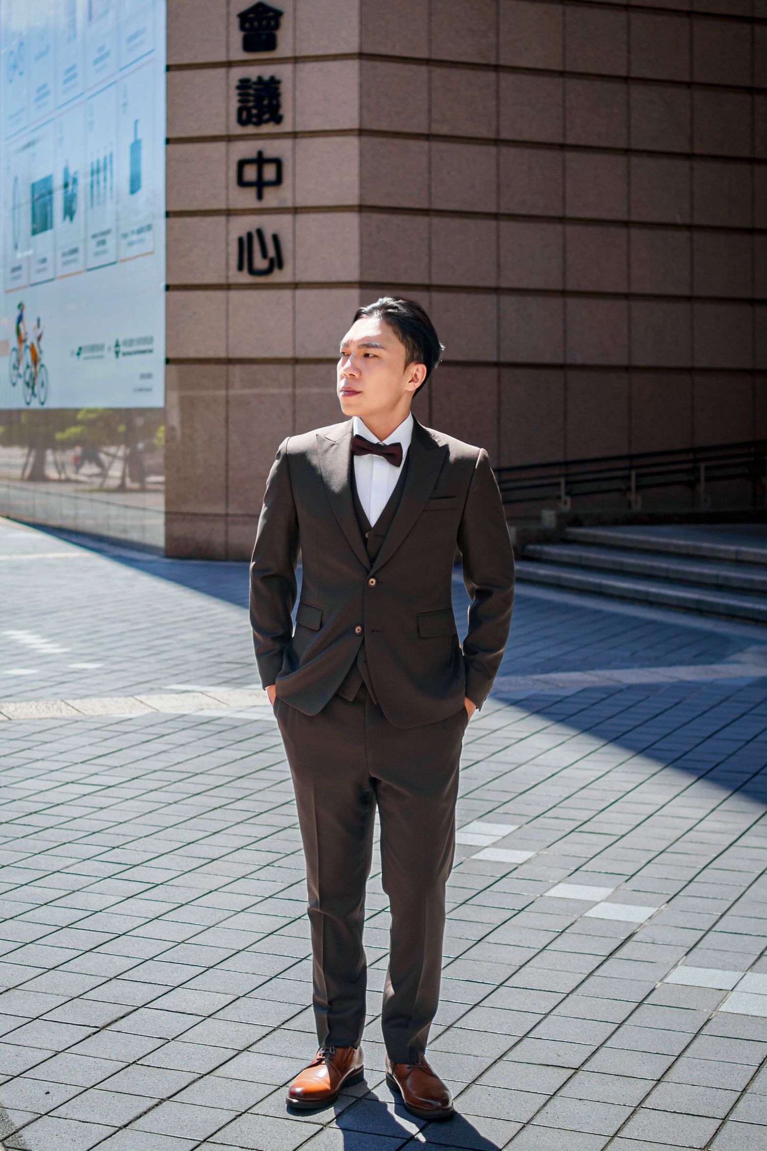 Professional wearing a dark suit stands in front of a modern building facade with Chinese characters.