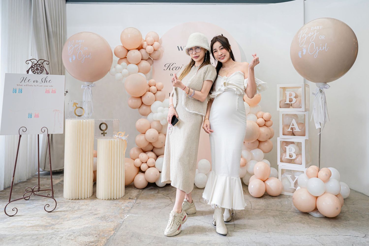 Elegant party setup with peach balloon arch, white candle pillars and decorative frames against light backdrop.