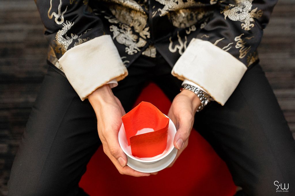Hands holding a ceremonial tea cup while wearing traditional Chinese formal attire.