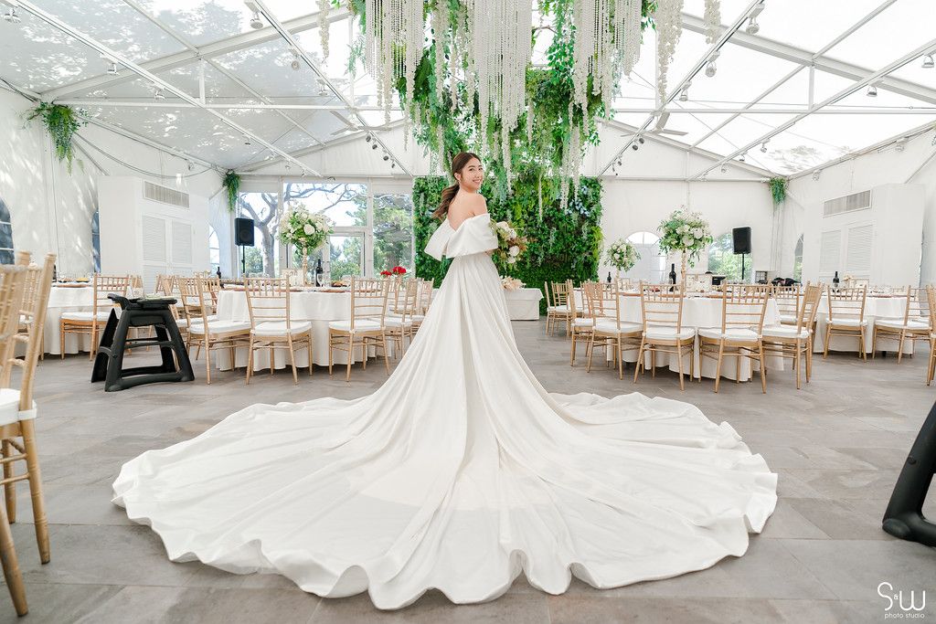 Dramatic long train wedding dress photographed in an elegant greenhouse venue with hanging plants.