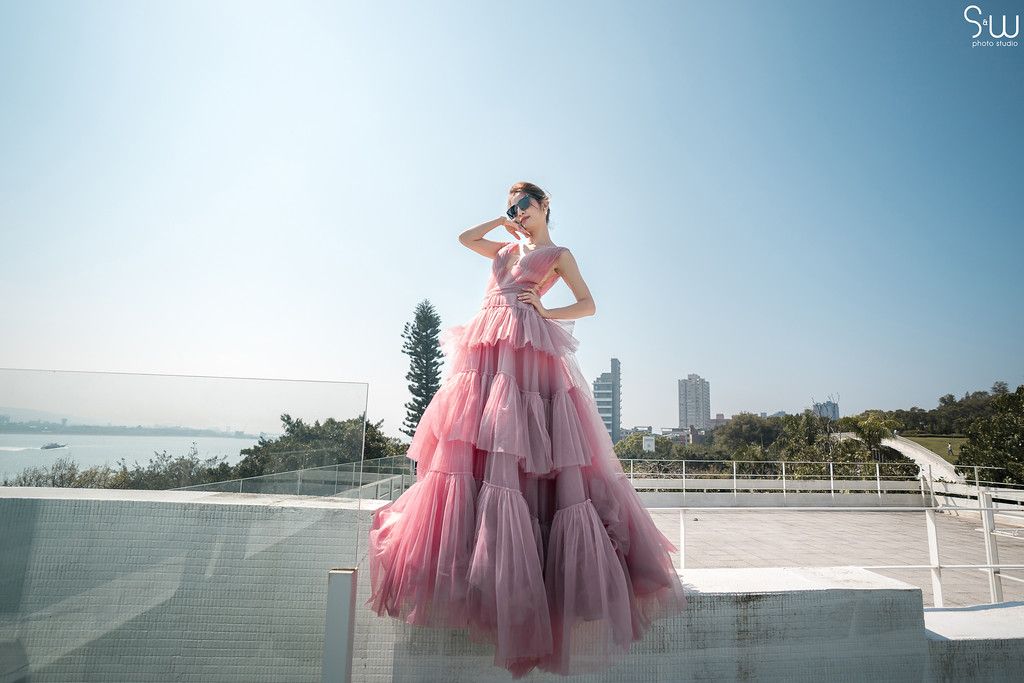 Pink tulle ballgown photographed against scenic waterfront backdrop on rooftop.