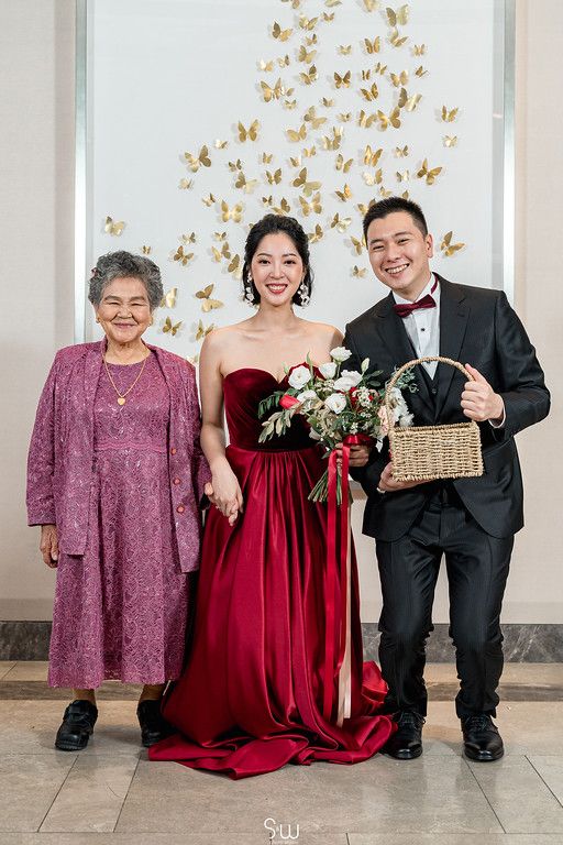 A formal portrait of a couple with an elderly relative in purple, standing against a butterfly wall display.