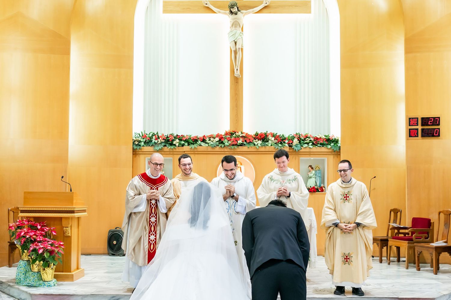 A bride and groom kneel before priests during a Catholic wedding ceremony.