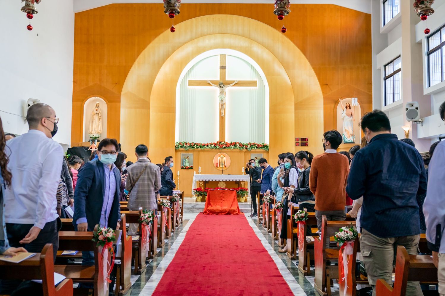 Interior of a church with yellow arch walls and large crucifix at altar during a wedding ceremony.