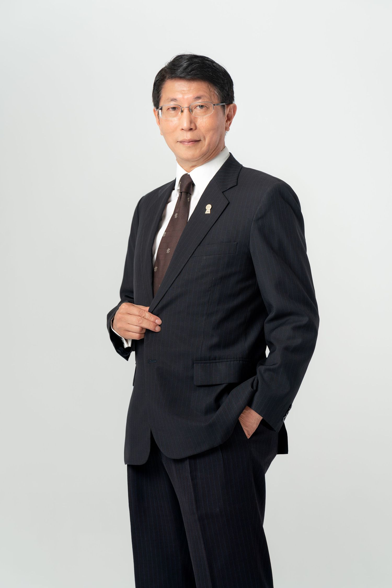 Professional business portrait of a person in a dark suit and glasses against a white background.