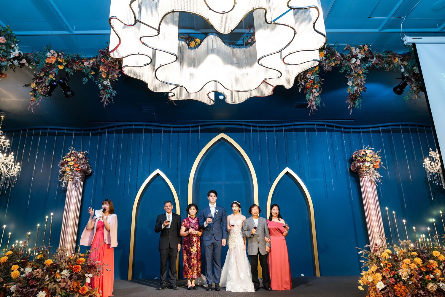 A wedding ceremony setup with a blue backdrop featuring Gothic-style arches, ornate floral arrangements, and decorative lighting.